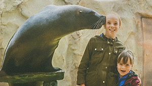 Zwei Kinder stehen neben der Seelöwenstatue im Conny Land, die den Kopf zu ihnen neigt.