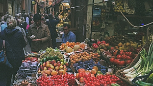 Gut besuchter Obstmarkt in Bologna in einer engen Gasse mit vielen verschiedenen Früchten.